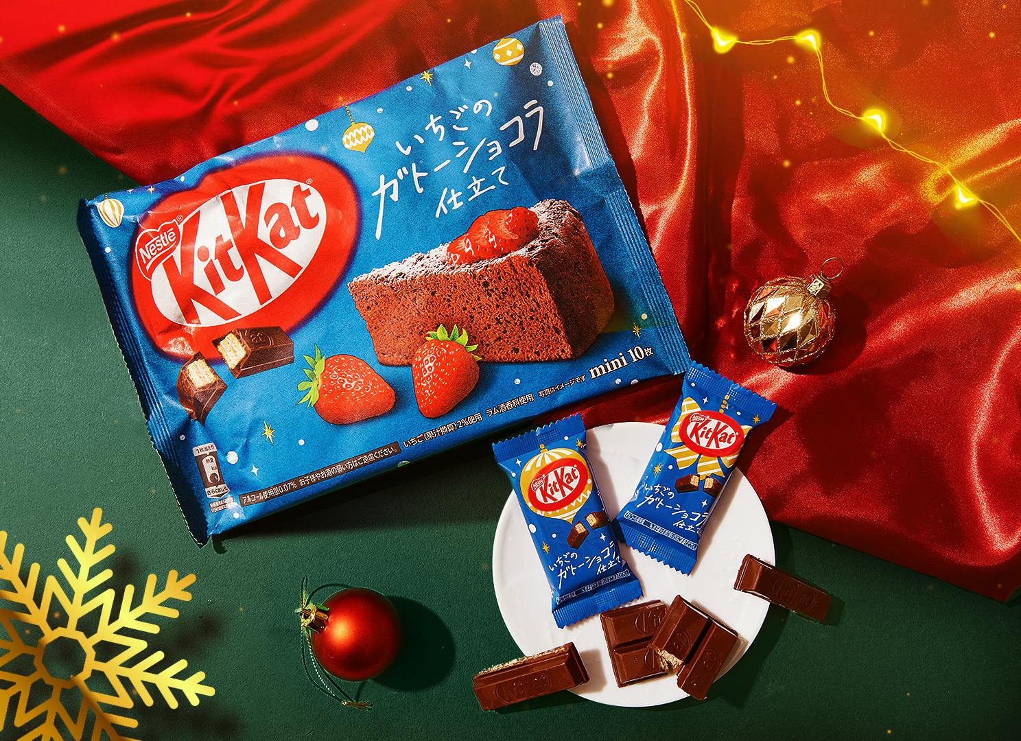 KitKat Strawberry Chocolate Cake snacks sit on a holiday green & red background, next to Christmas lights and snowflake ornaments. KitKat Strawberry Chocolate Cake snacks sit on a holiday green & red background, next to Christmas lights and snowflake ornaments.