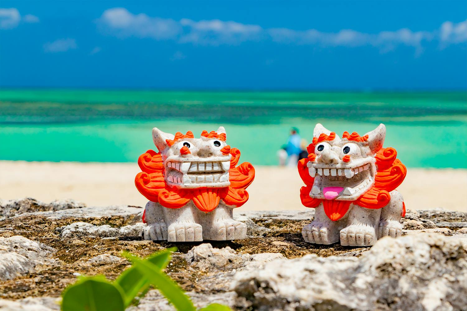 Two red and grey stone shisa sit on a beach in Okinawa.