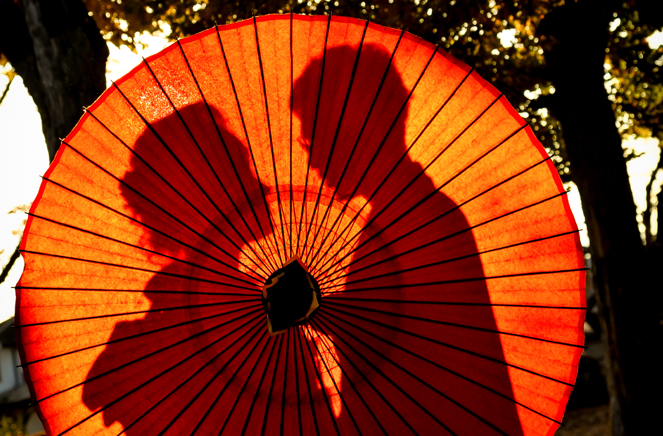 A man and woman hiding behind a paper umbrella.