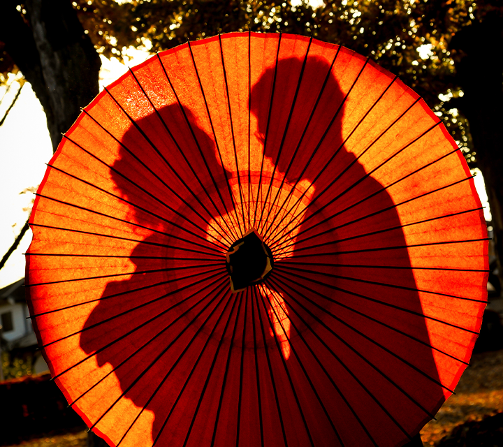 A man and woman hiding behind a paper umbrella.