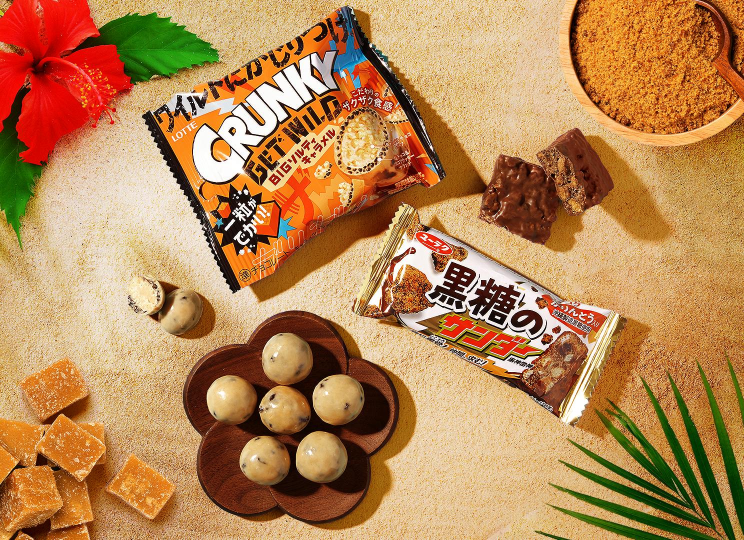 Crunky Salty Caramel Bites and Kokutou Black Thunder snack items sit on an Okinawan beach.