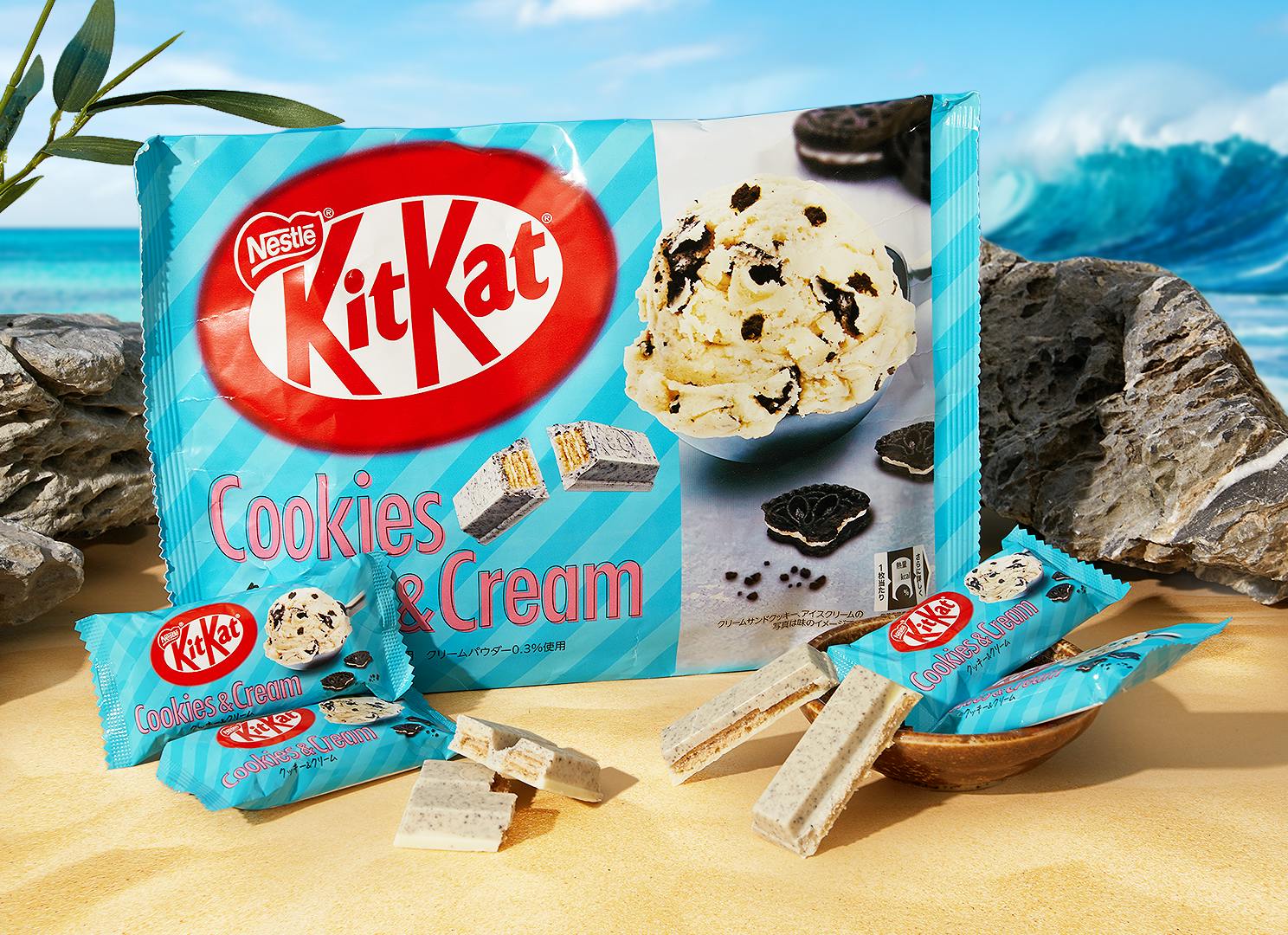 KitKat Cookies & Cream item sits on a soft, sandy beach in Okinawa, surrounded by blue waves, sea rocks, and greenery.