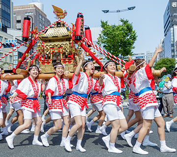 A  group of Japanese women in happi coats are carrying a portable shrine at a Japanese matsuri festival