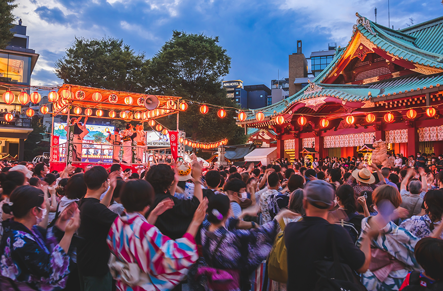 A crowd of festival-goers dance in a circle at a Japanese summer festival.