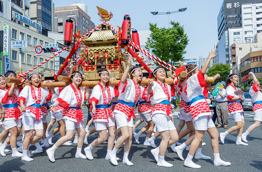 A  group of Japanese women in happi coats are carrying a portable shrine at a Japanese matsuri festival