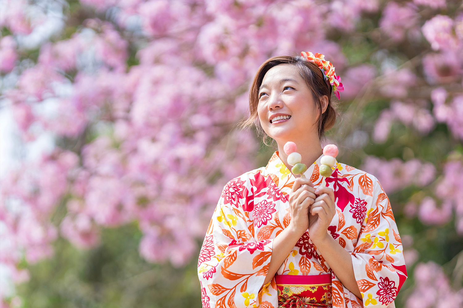 A woman dressed in a yukata holds dango in her hands.