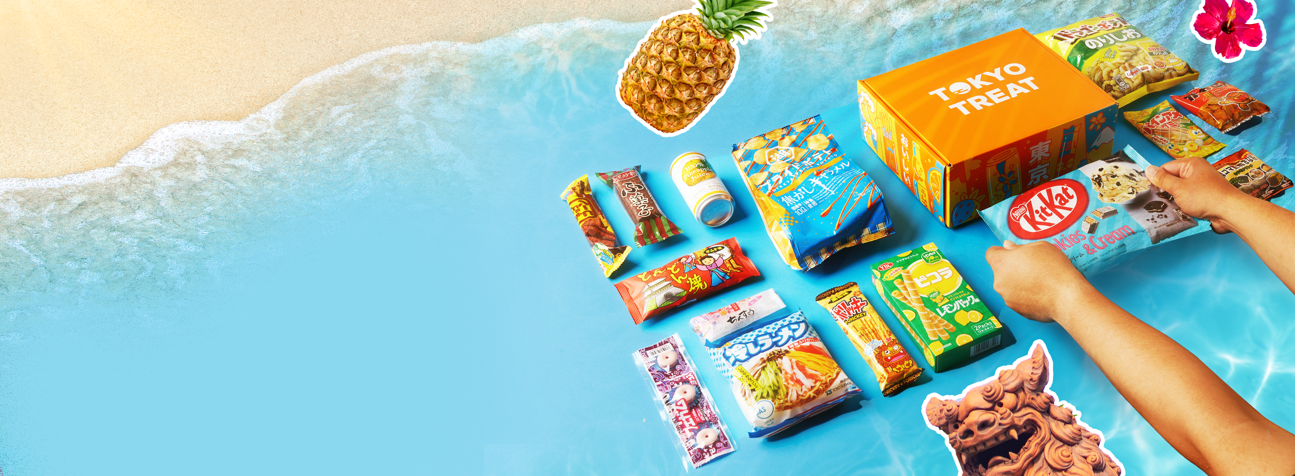 TokyoTreat box sits on a white-sand, blue-water Okinawa beach, surrounded by box items.