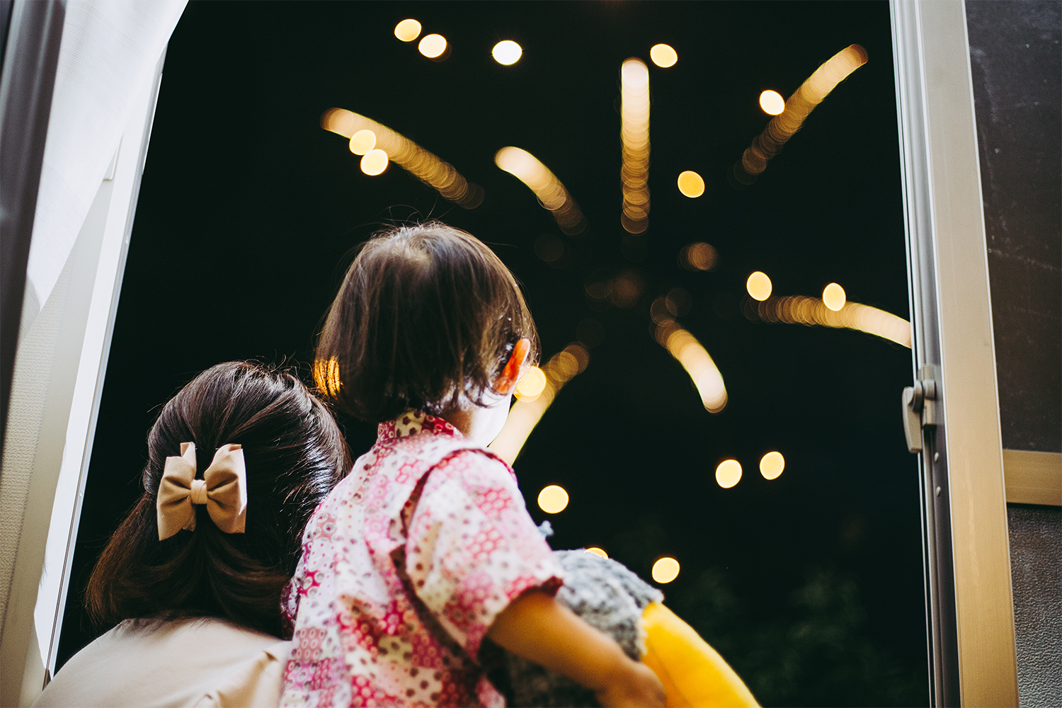 A young family in Tokyo look up at nighttime fireworks in the sky.
