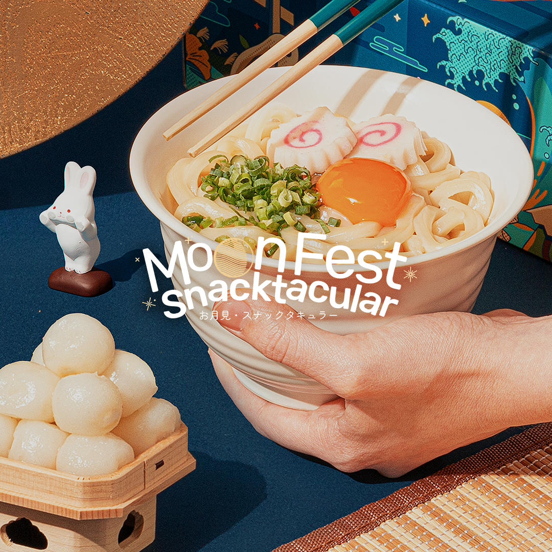 A pair of hands hold a bowl of Tsukimi udon, surrounded by Japanese Moon Festival decor.