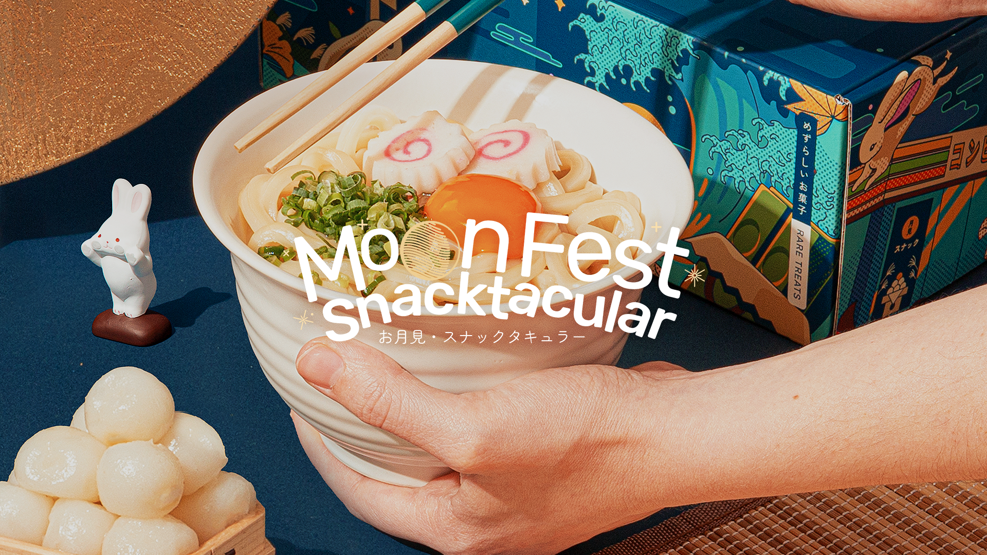 A pair of hands hold a bowl of Tsukimi udon, surrounded by Japanese Moon Festival decor.