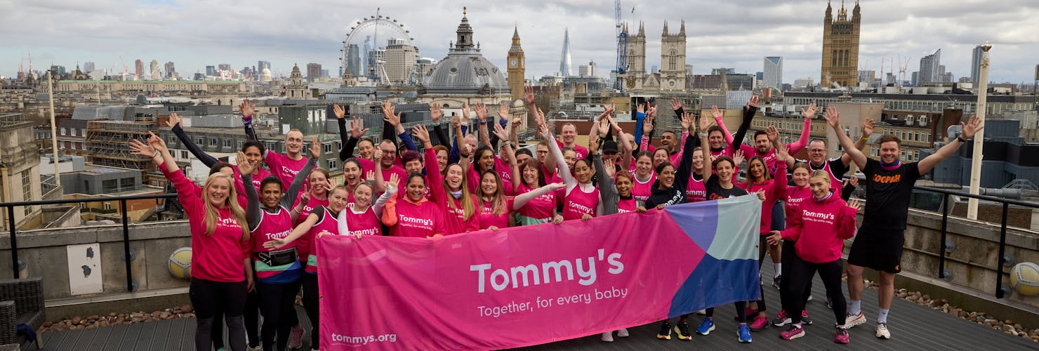 Women running the LLHM wearing a pink tommy's top, high-fiving the cheerers on the side of the road