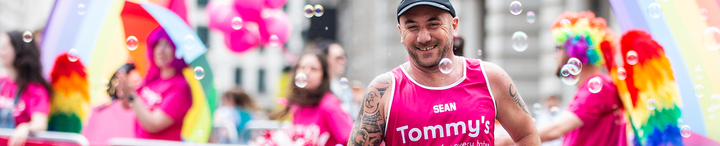 Tommy's supporter running past the Tommy's rainbow cheer station in the LLHM with a Tommy's pink vest.