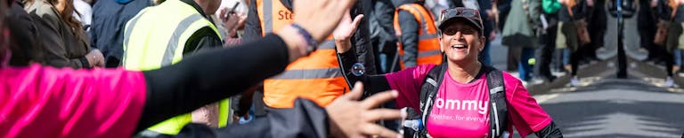 Women running the LLHM wearing a pink tommy's top, high-fiving the cheerers on the side of the road