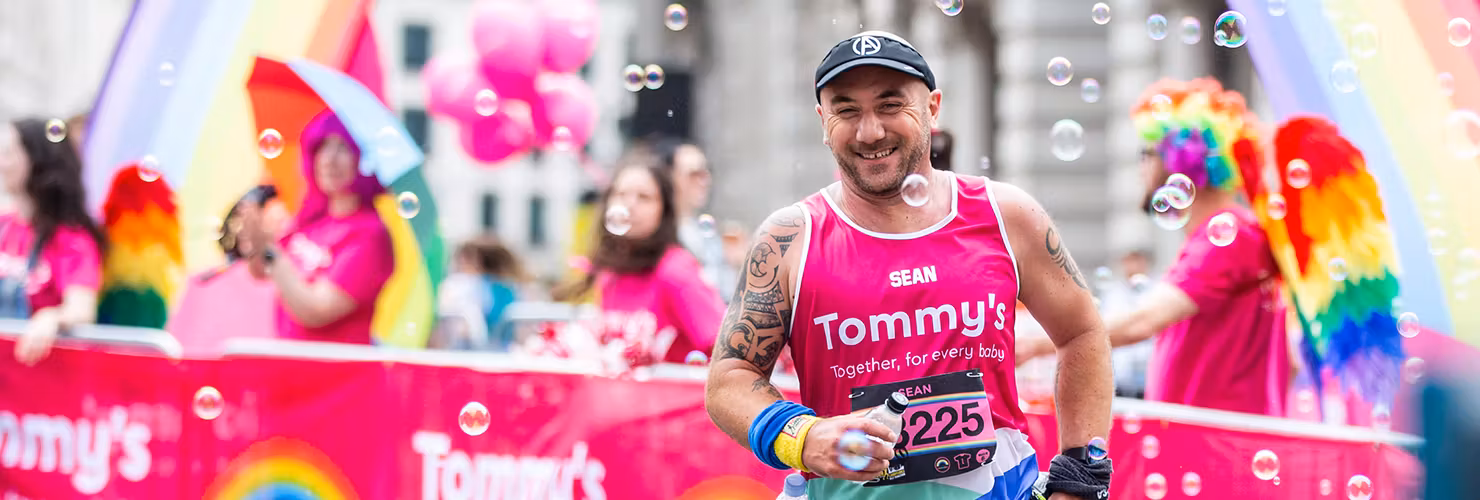 Tommy's supporter running past the Tommy's rainbow cheer station in the LLHM with a Tommy's pink vest