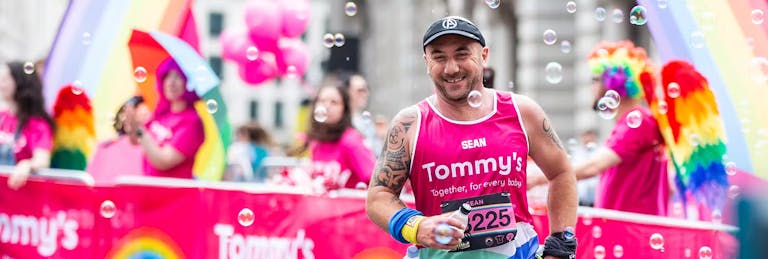 Tommy's supporter running past the Tommy's rainbow cheer station in the LLHM with a Tommy's pink vest