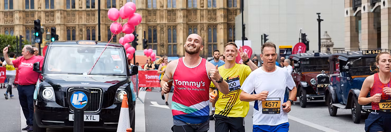 Runners with a black cab behind them with pink balloons