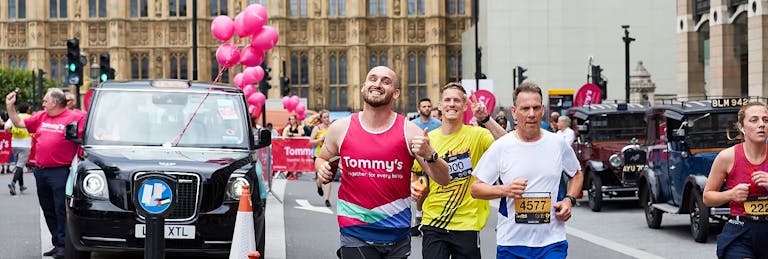 Runners with a black cab behind them with pink balloons