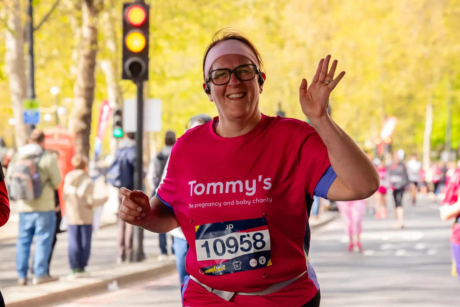 Runner in red Tommy’s shirt waves while running past traffic lights on city street.