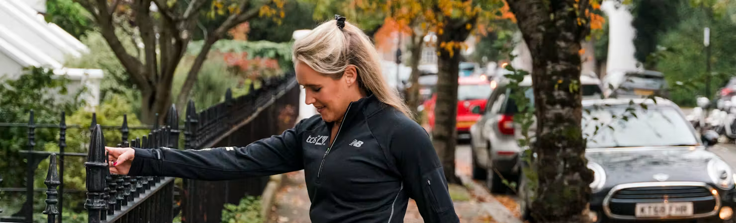 Woman dressed in all black holding fence whilst stretching leg.