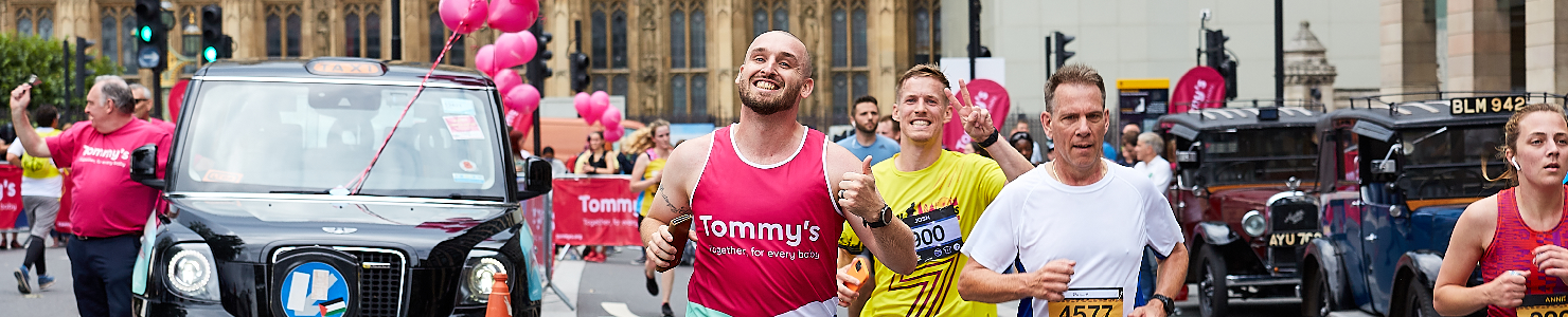 Runners with a black cab behind them with pink balloons.