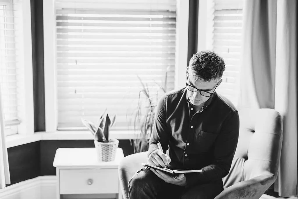 Tony taking notes sitting in a chair in his counselling room in Devon