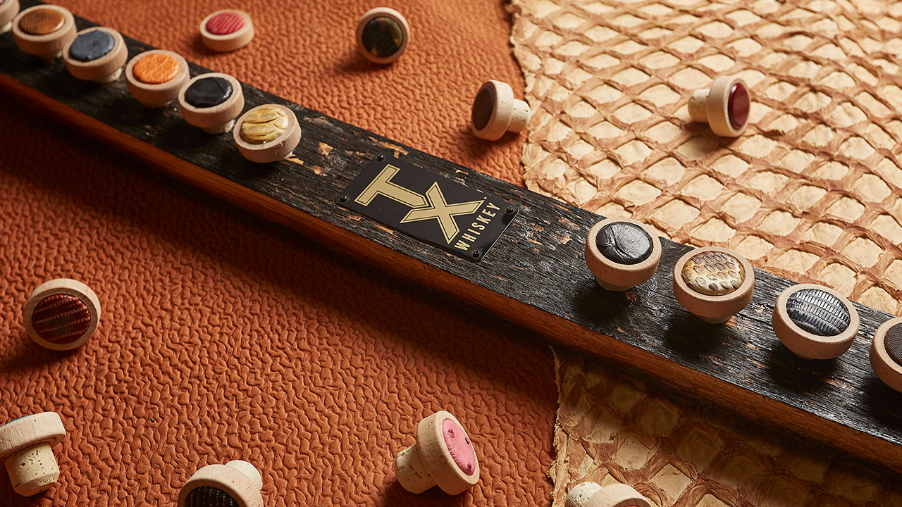 Row of bottle caps on a wooden board labeled with the TX logo sitting on top of Tony Lama leathers.