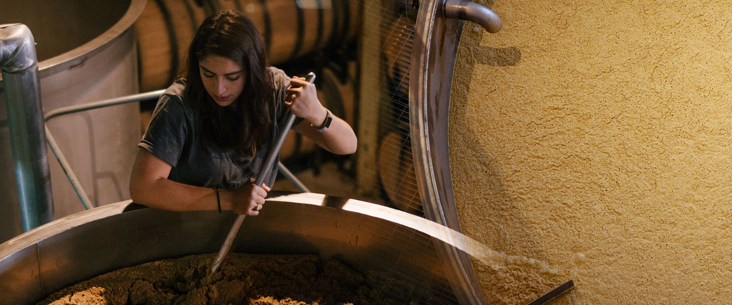 Worker mixes ingredients in large vat split on screen with a close-up of ingredients in vat.