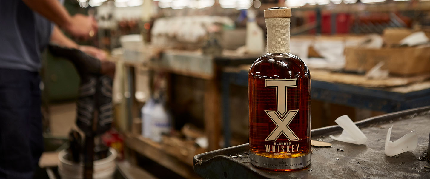 TX Whiskey bottle on cart as Tony Lama worker works on boot in background.