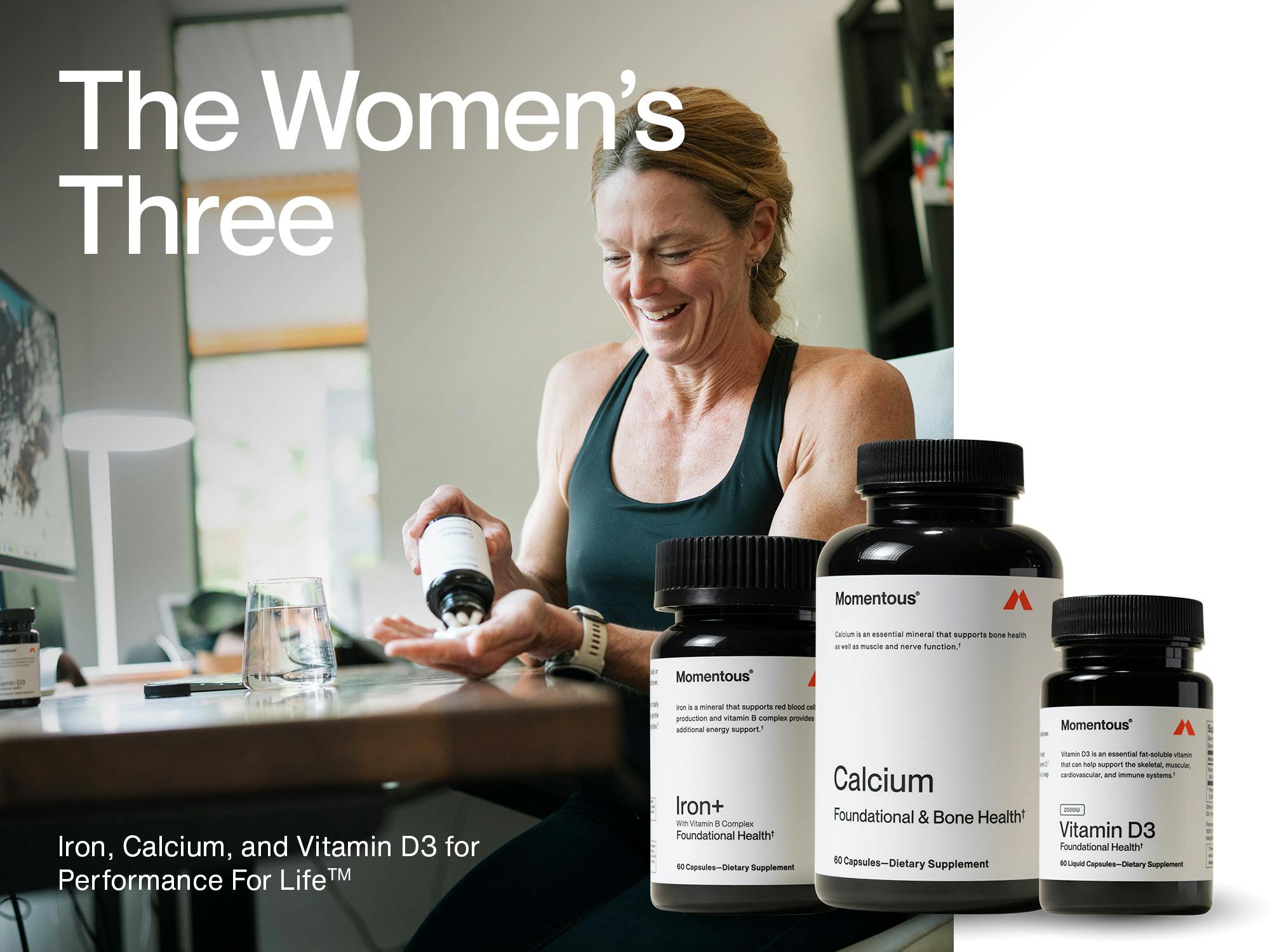 A fit, smiling woman in a sleeveless top sits at a desk and pours capsules from a supplement bottle into her hand. On the desk are a glass of water and a computer. Superimposed on the image are three supplement bottles labeled "Momentous Iron+," "Momentous Calcium," and "Momentous Vitamin D3." Large text reads "The Women’s Three." Smaller text below says "Iron, Calcium, and Vitamin D3 for Performance For Life™."