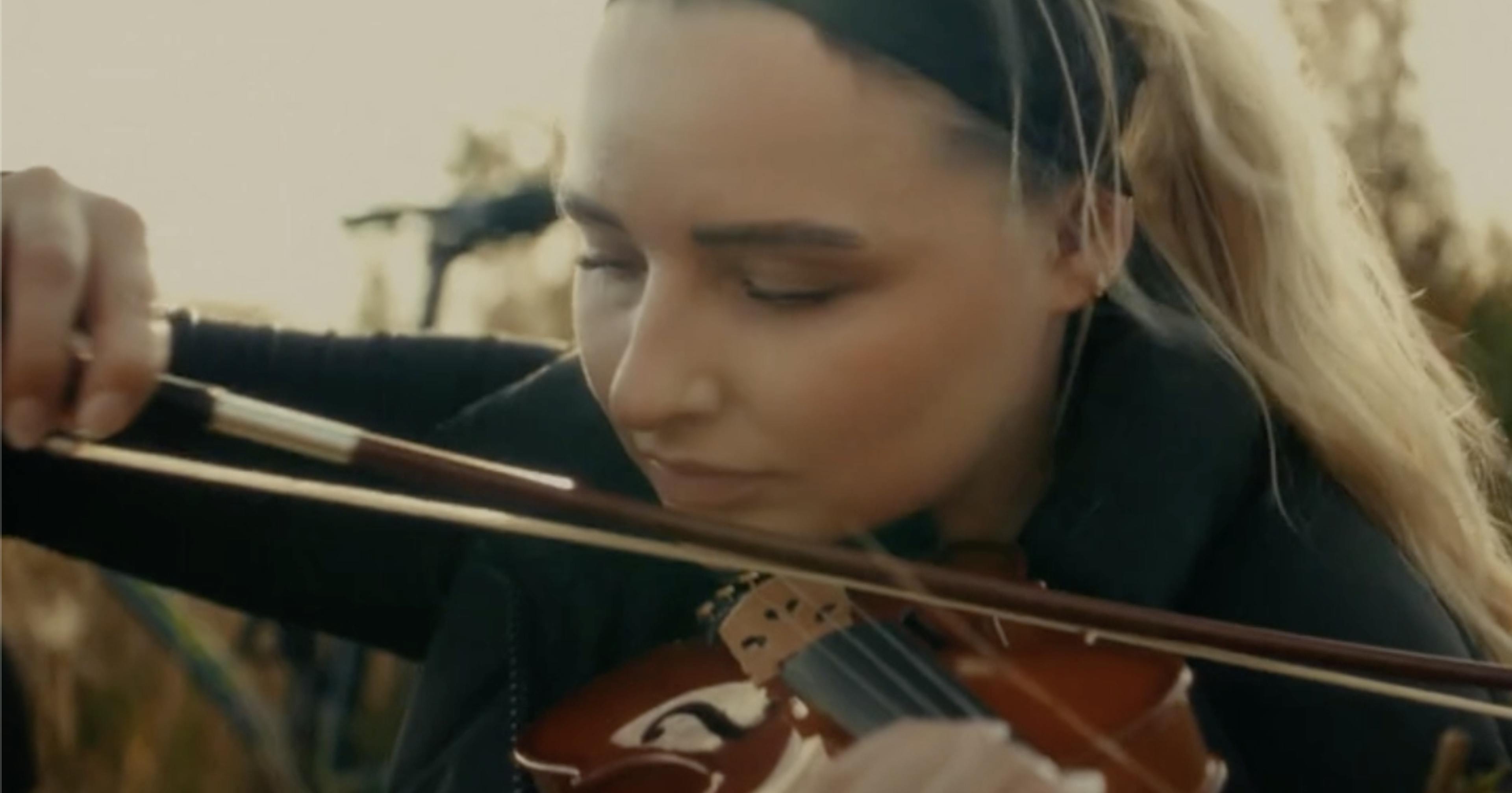 Girl in field playing violin bike in background