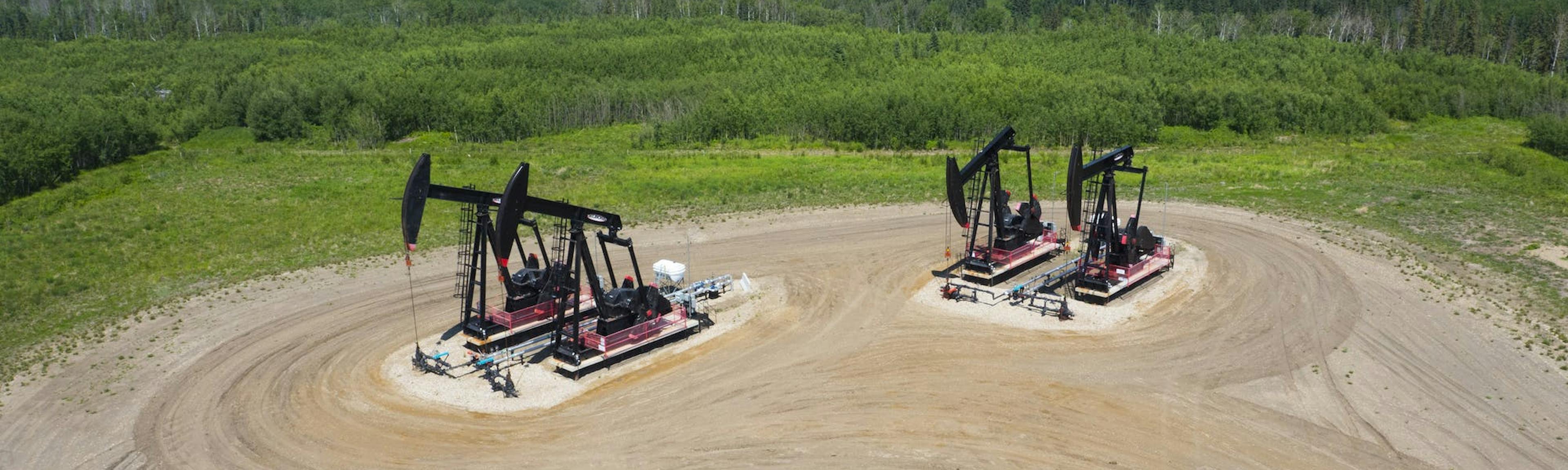 An aerial view of a pump jacks, with green fields and forests in the background.