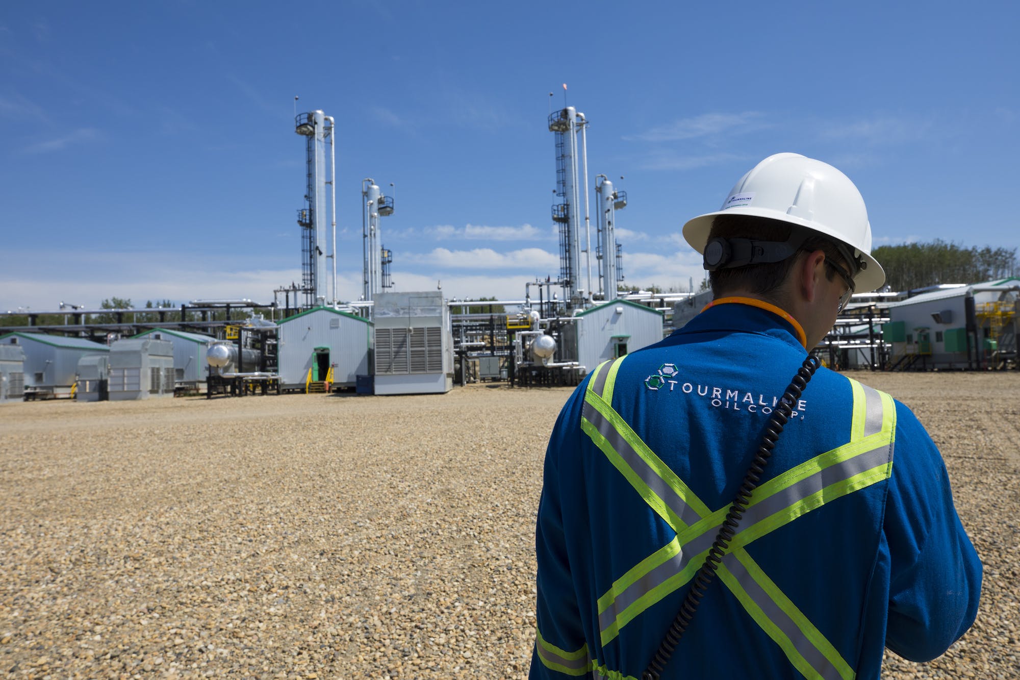 An over-the-shoulder view of a gas plant worker assessing operations from afar.
