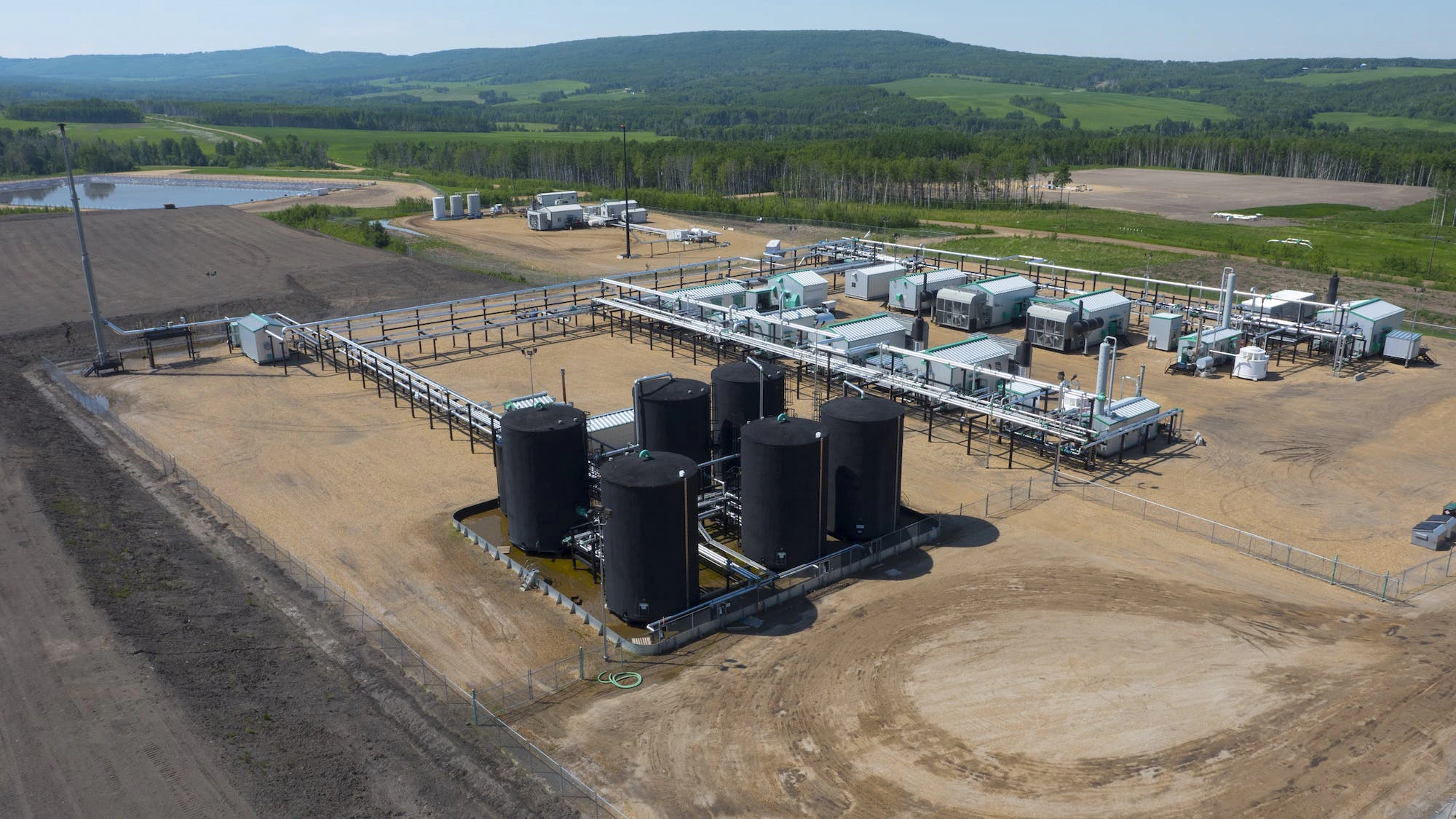 An aerial view of a gas plant, with a small pond in the background.