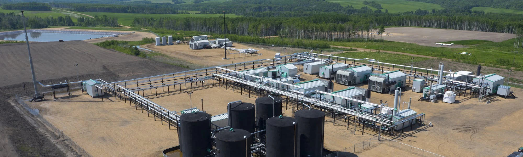 An aerial view of a gas plant, with a small pond in the background.