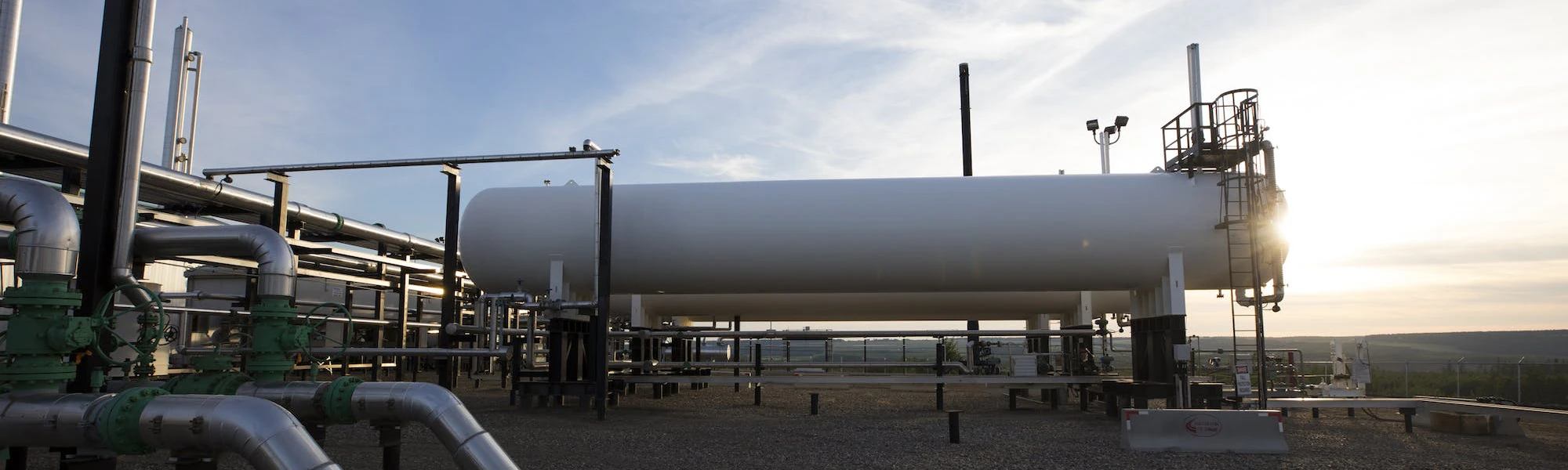 A large white tank at a gas plant, backlit by the sun.