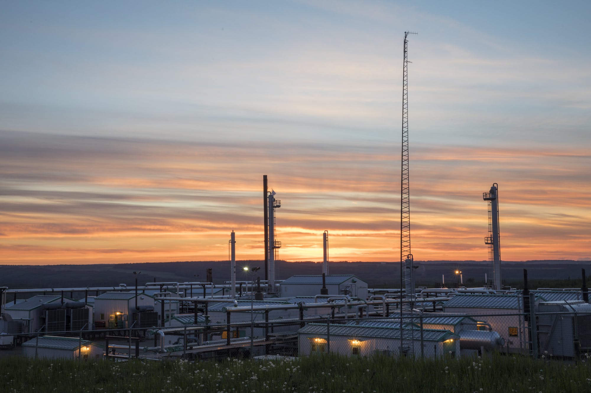 A gas plant backlit by a vivid orange and purple sky.