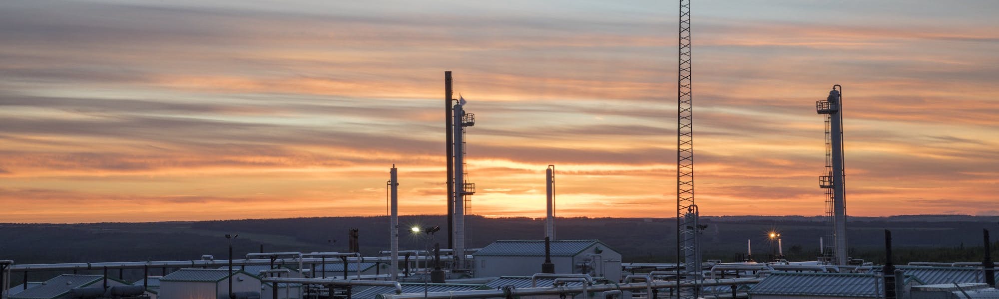 A gas plant backlit by a vivid orange and purple sky.