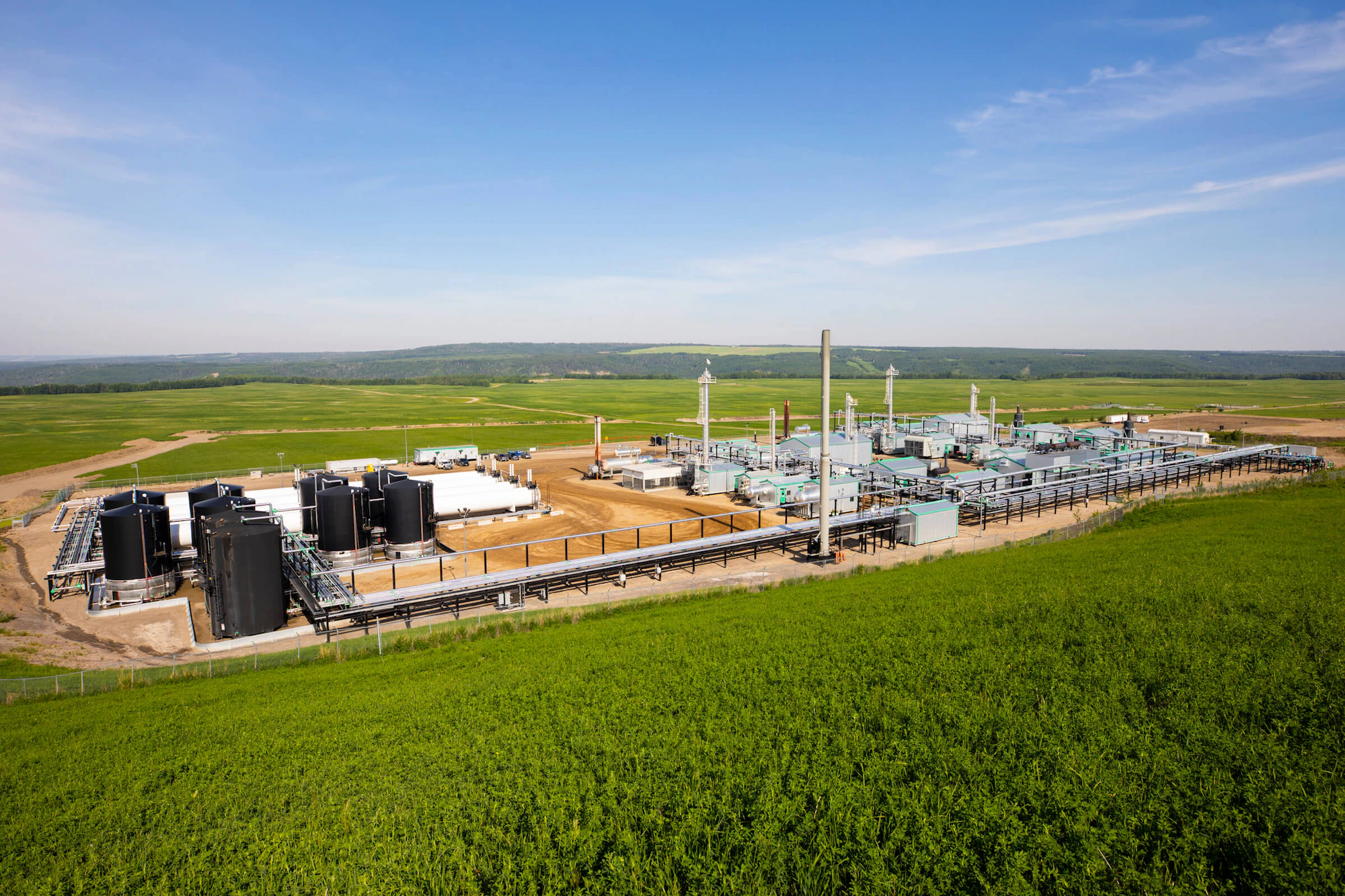 A gas facility in a green field, under a blue sky.
