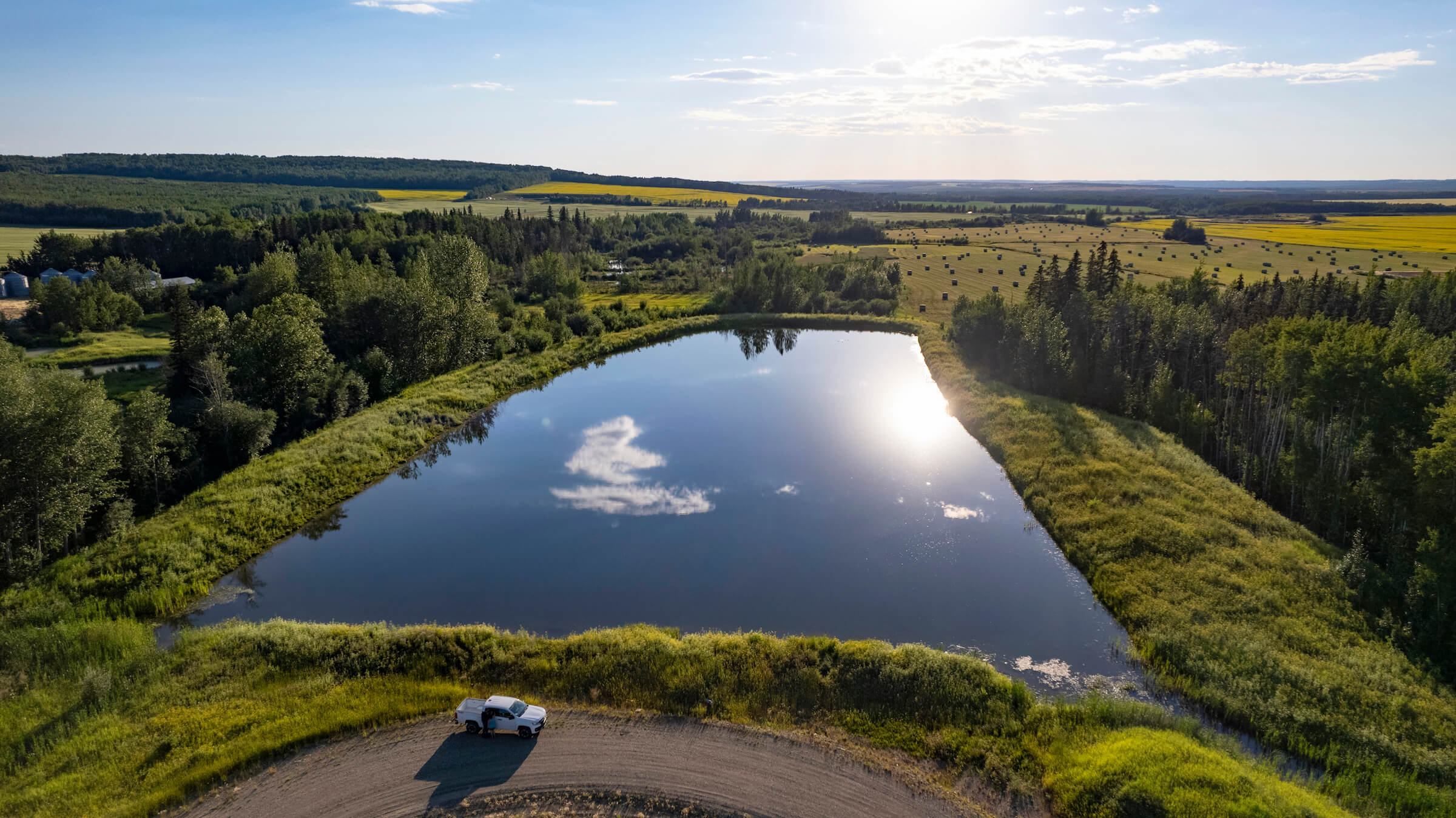 A white truck parked next to a man-made lake in a green field.