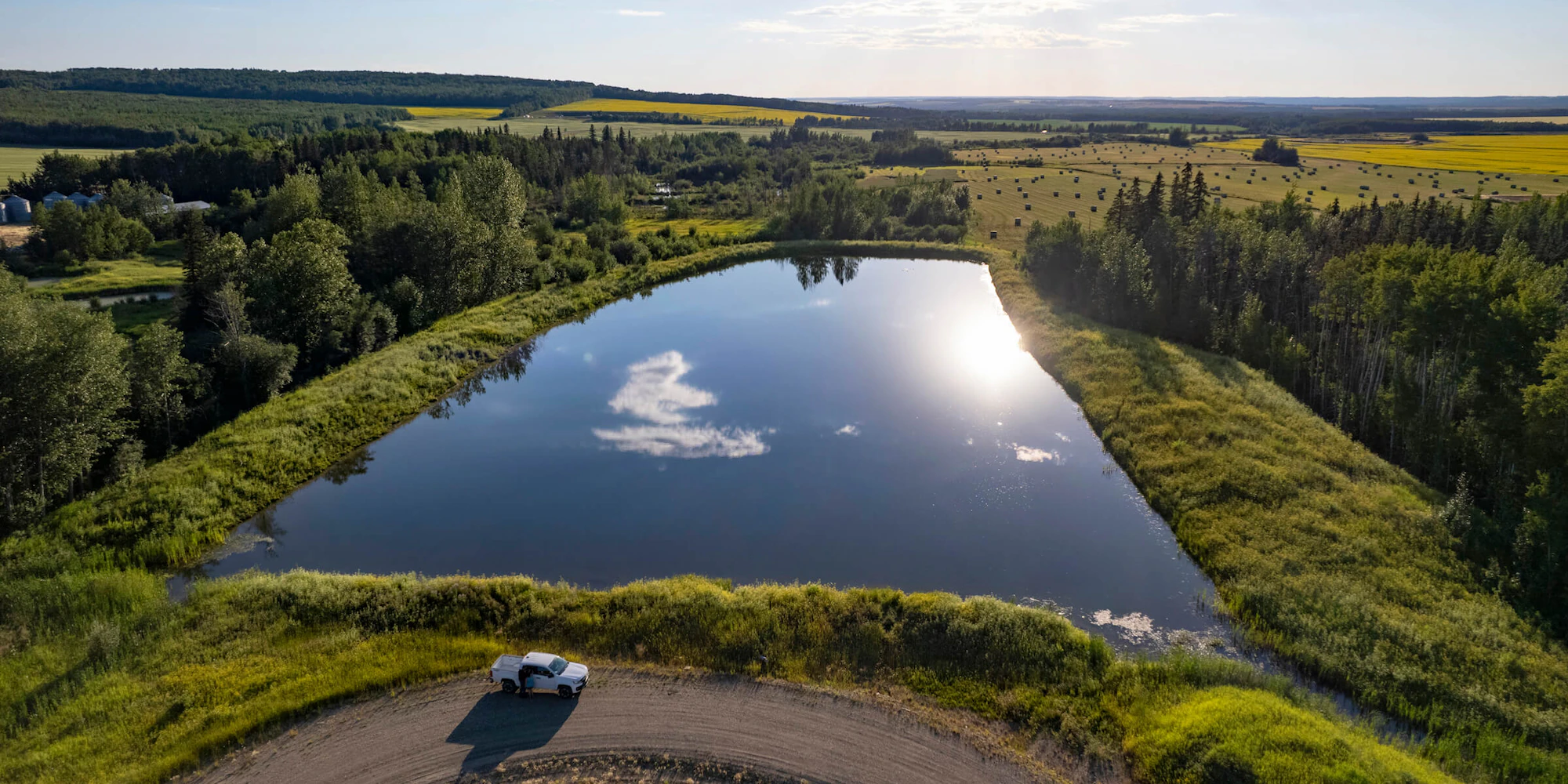 A white truck parked next to a man-made lake in a green field.