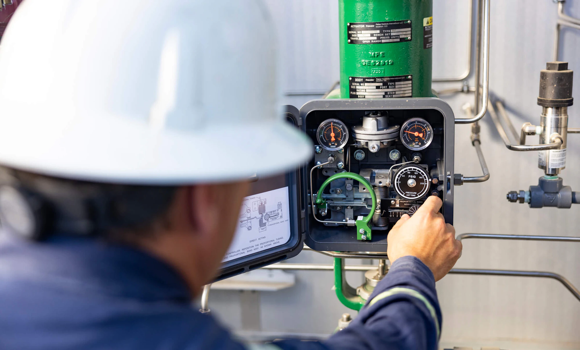 A worker in blue coveralls and a white hard hat adjusts dials on gas equipment.