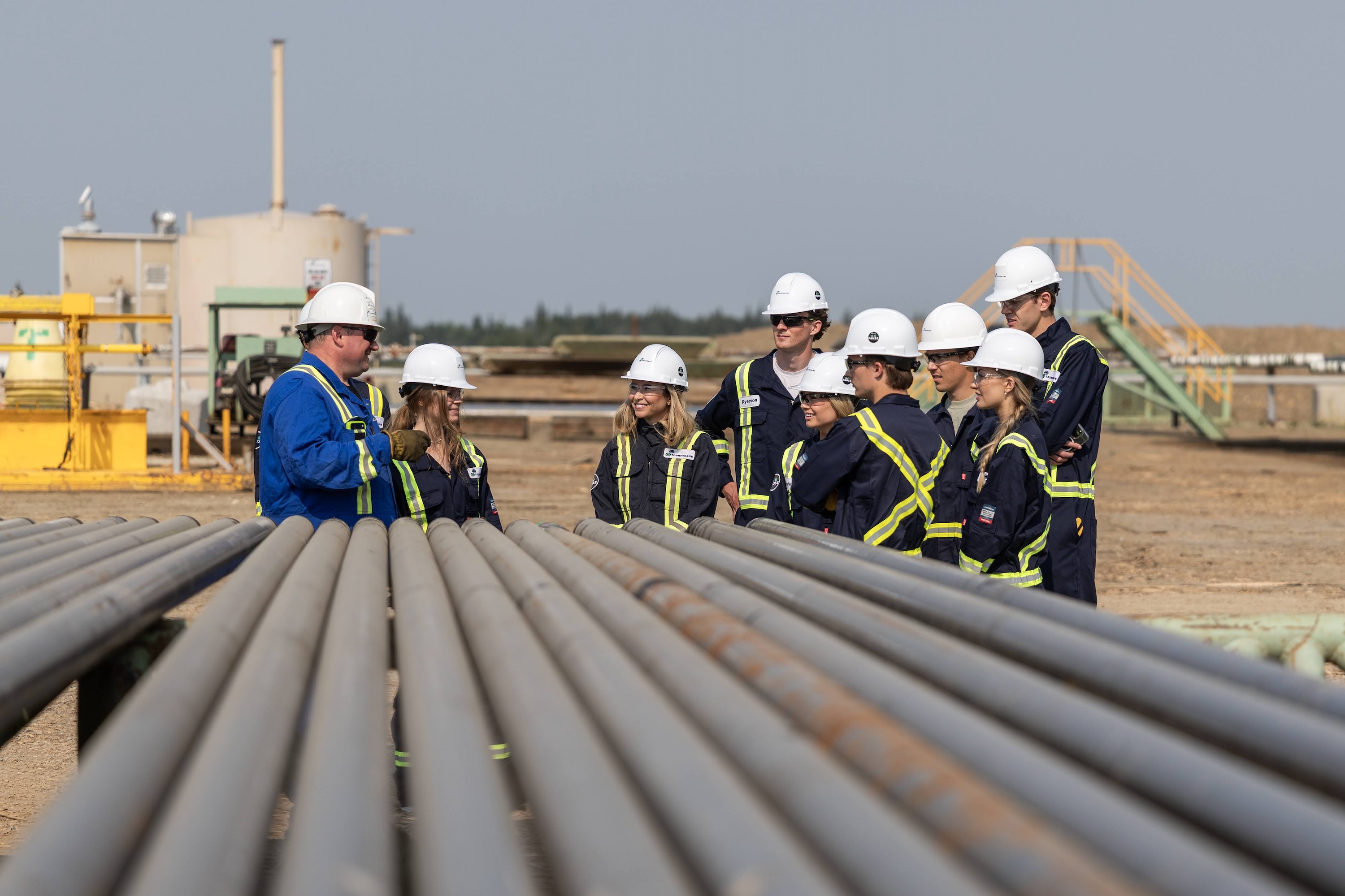 A group of summer students discuss work on-site with experienced professionals at a gas plant.