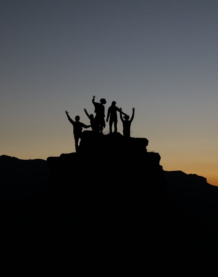 A silhouette of 5 people on the top of a hill at dusk
