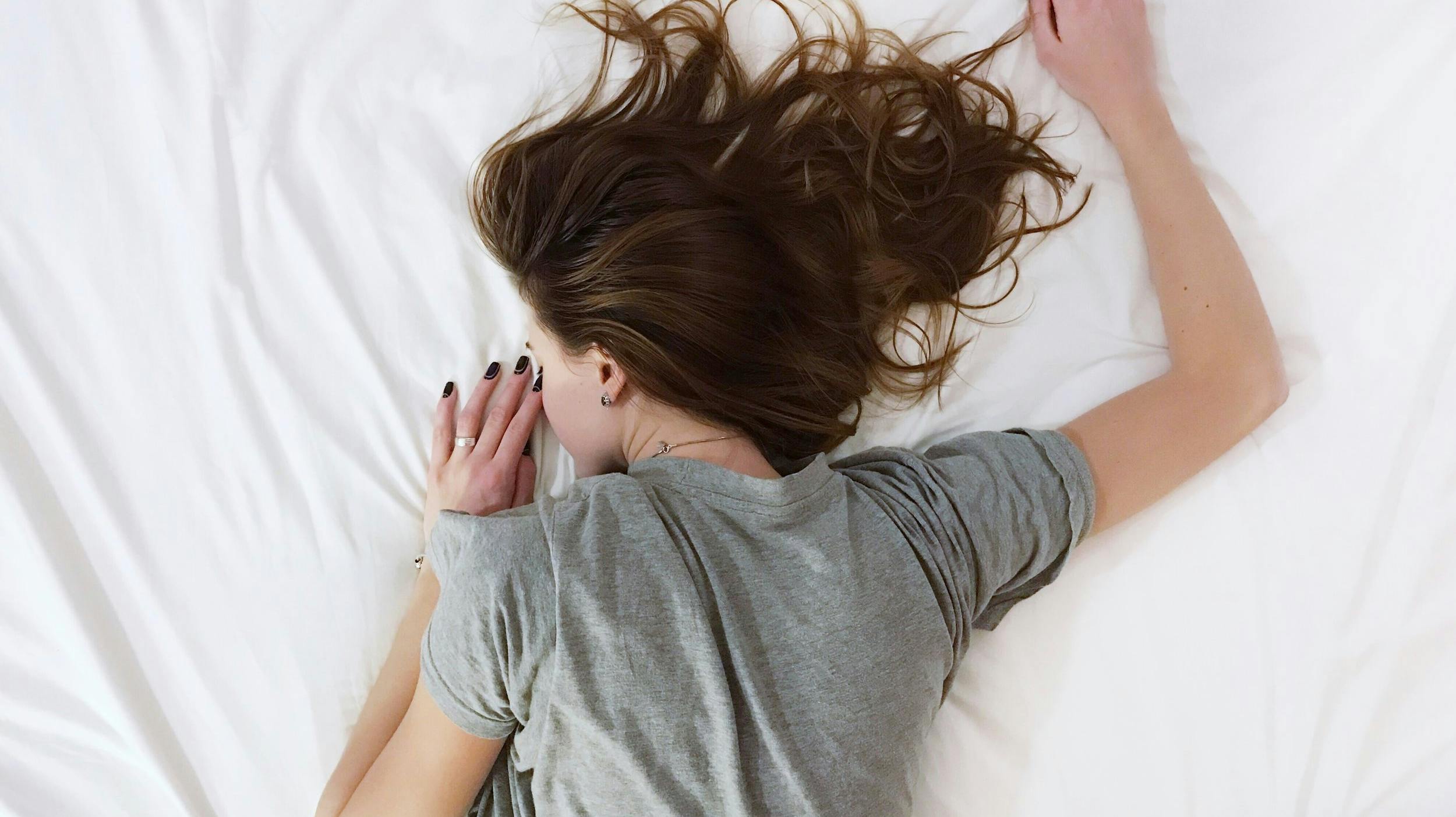 Woman wearing gray shirt laying face down in bed