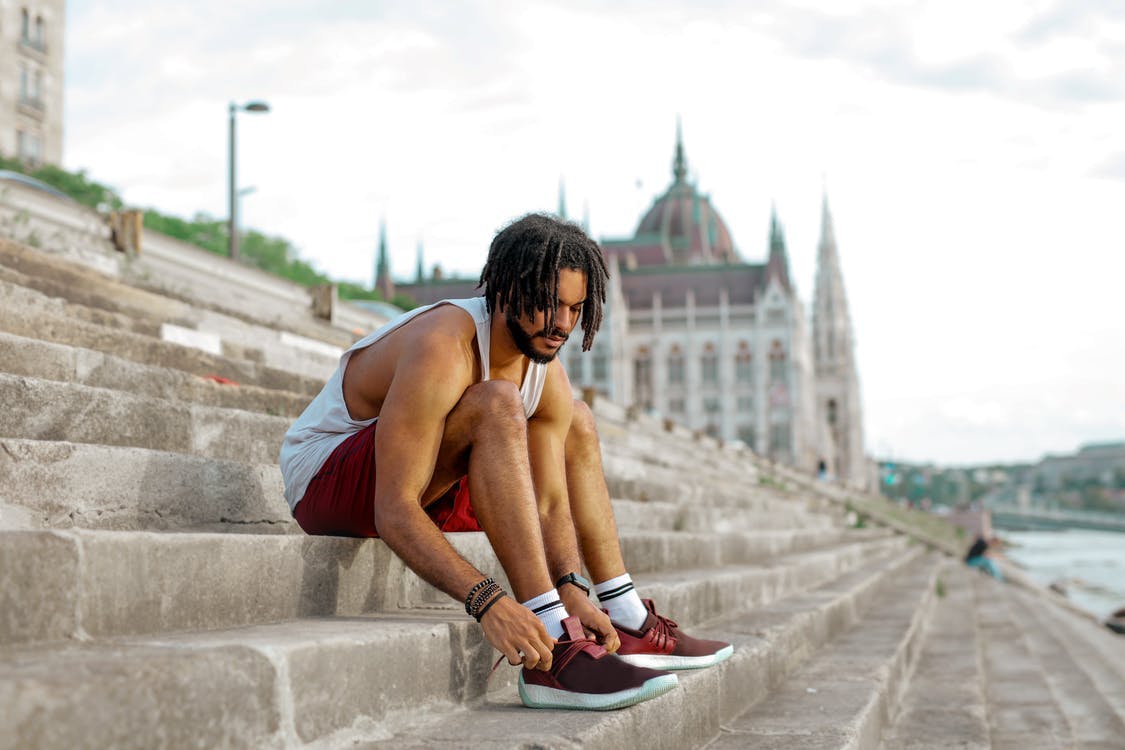 man sitting on cement stairs tying his shoes about to workout 