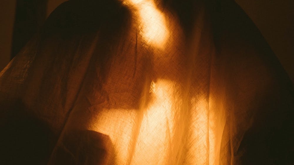 A backlit image of a couple sharing an intimate kiss, under a linen blanket.
