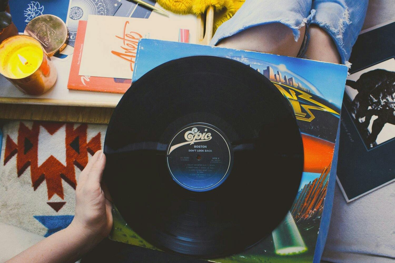 Woman in torn jeans sitting with a vinyl record in her lap.