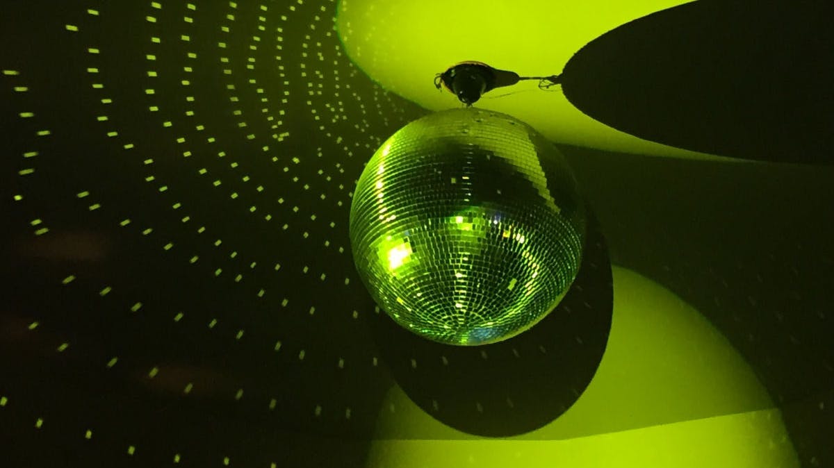 A disco ball glistening and bouncing light in a green hued environment. 