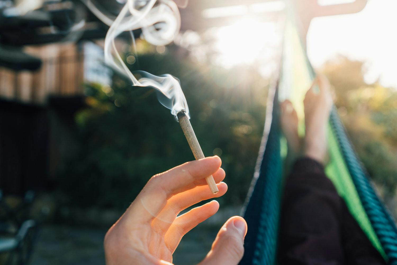 Person sitting in hammock smoking a marijuana cigarette.