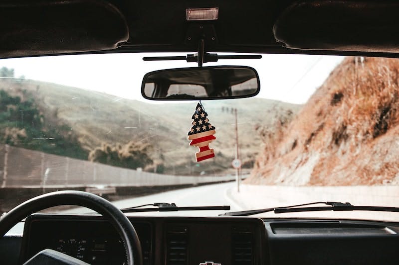 An all-American road trip featuring a majestic rocky road with an American flag-emblazoned car air freshener hanging from the rearview mirror. 